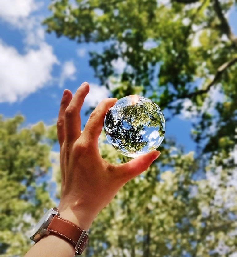 Man holding glass orb up to trees and sky